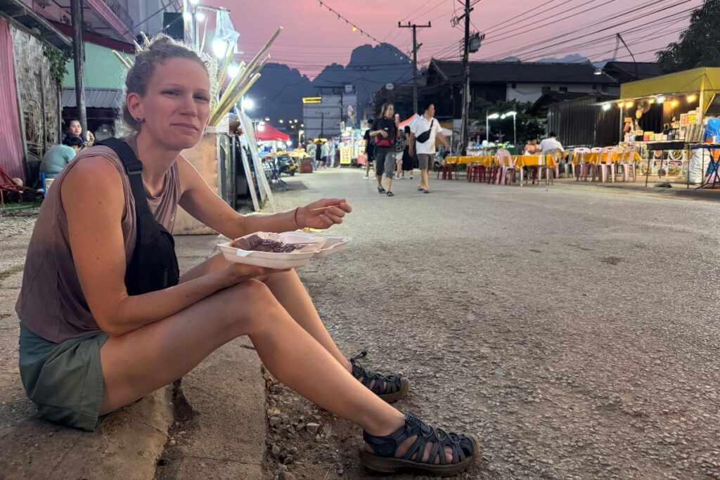 woman sitting on a curb at a night market eating