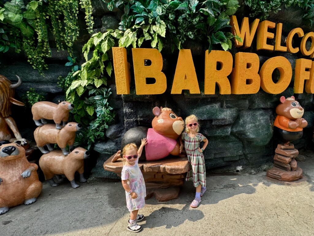 two girls posing with sunglasses in front of a cartoon statue