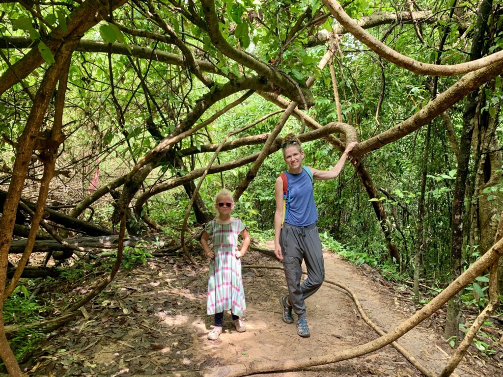 mother and child taking a picture on a trail with large vines crossing over the trail