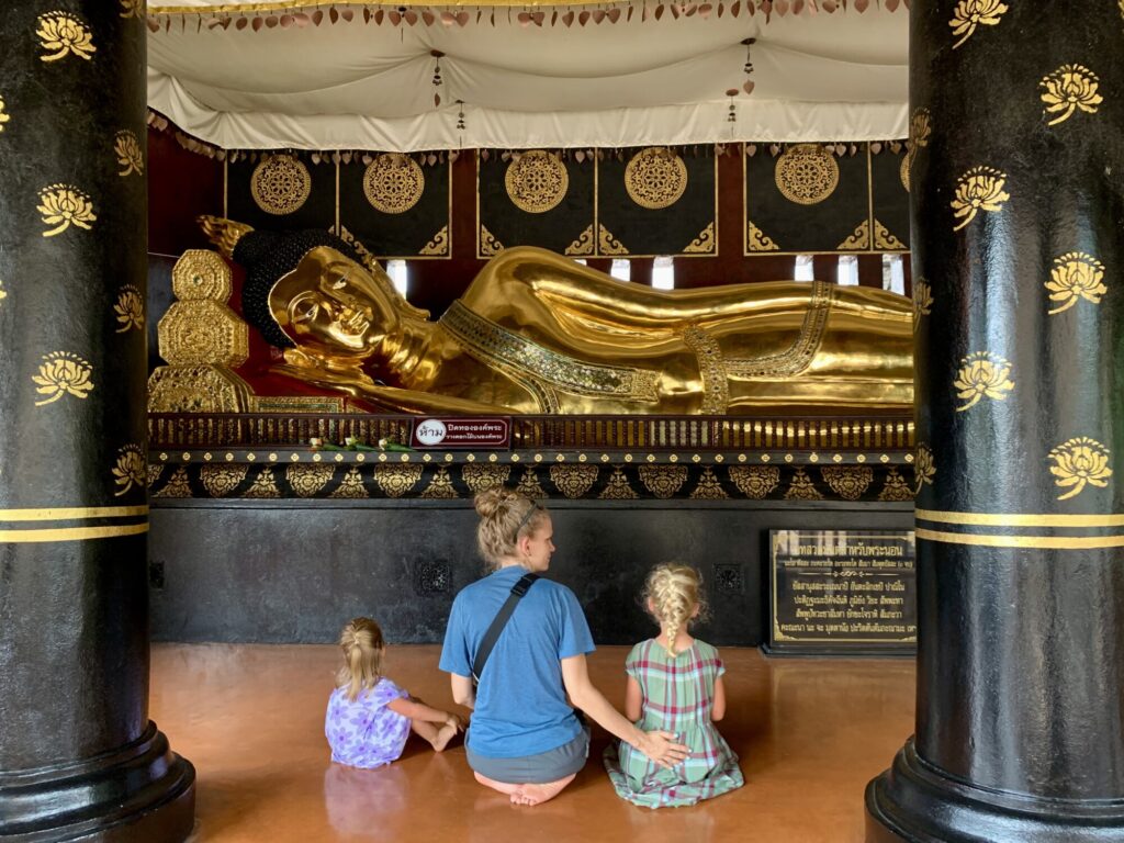 two girls and a mom sitting in front of a reclining Buddha