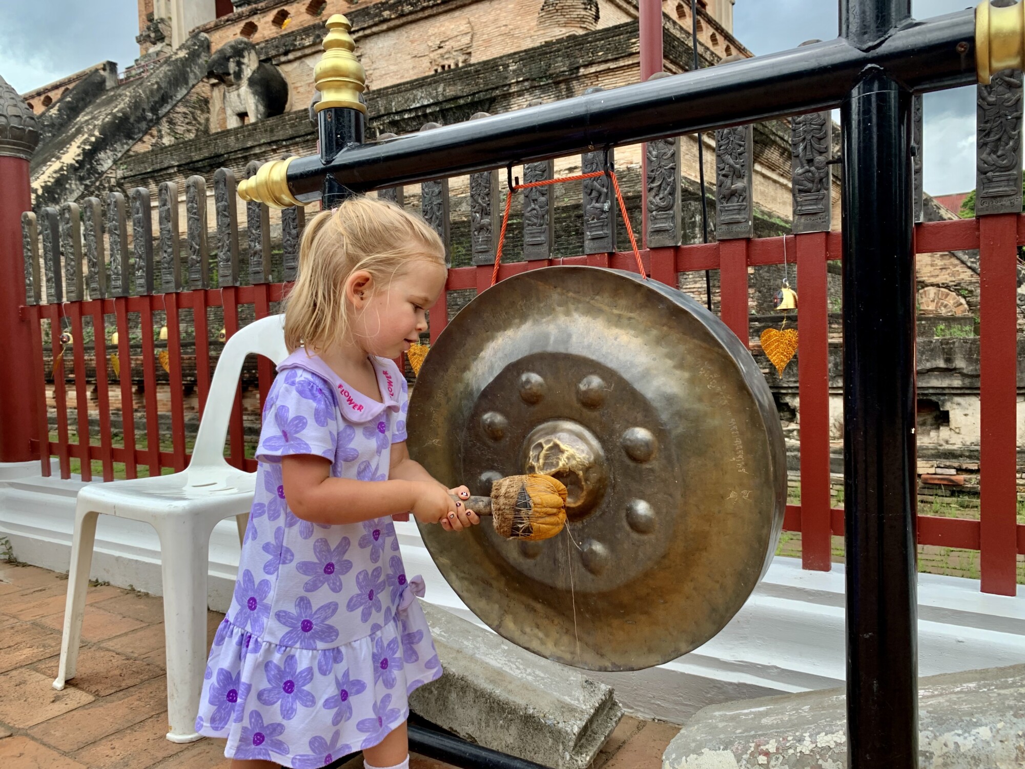 girl hitting a gong outside of a temple