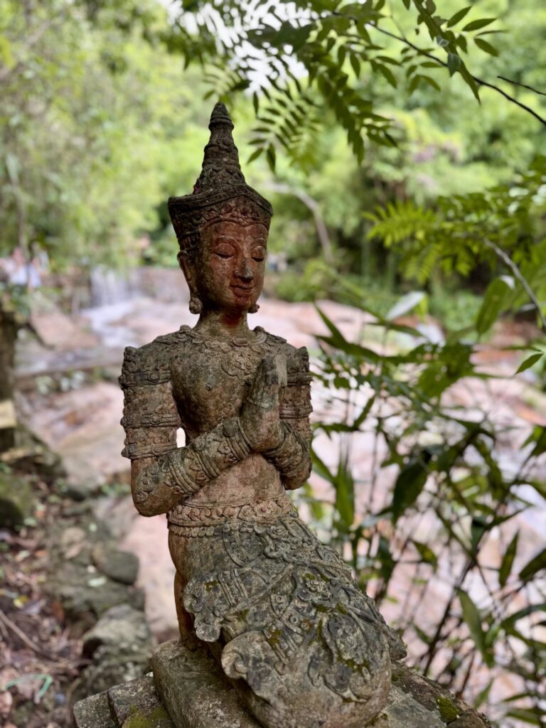 a Buddha statue that is praying with a stream in the background