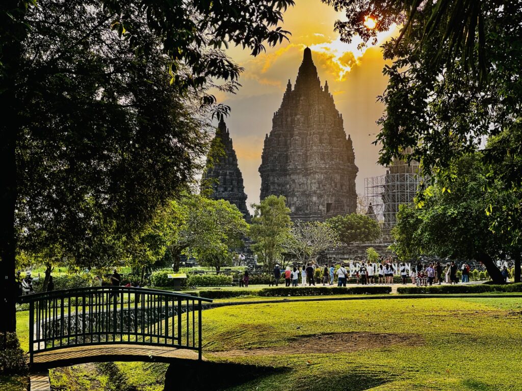 sun setting behind a temple with a grassy foreground and a small bridge