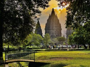 sun setting behind a temple with a grassy foreground and a small bridge