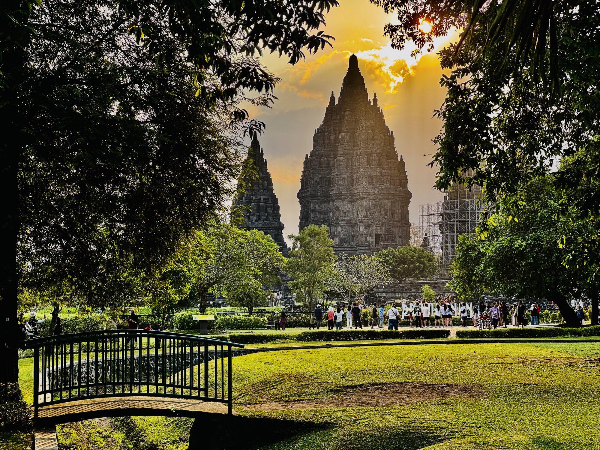 sun setting behind a temple with a grassy foreground and a small bridge