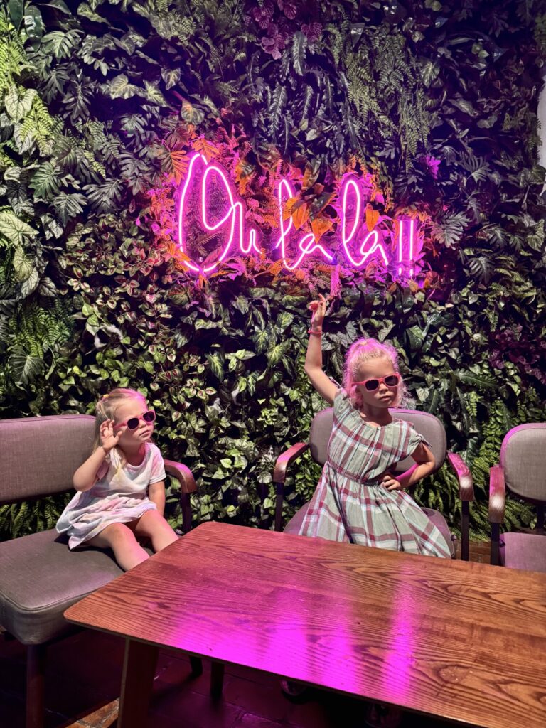 two girls posing under a pink fluorescent sign