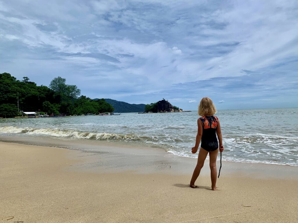 girl standing on a beach watching the waves while holding a stick