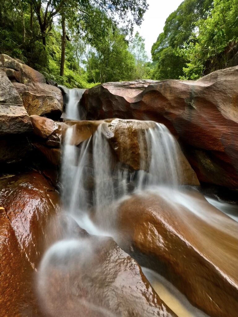 waterfall gently flowing over red iron colored rock in the jungle