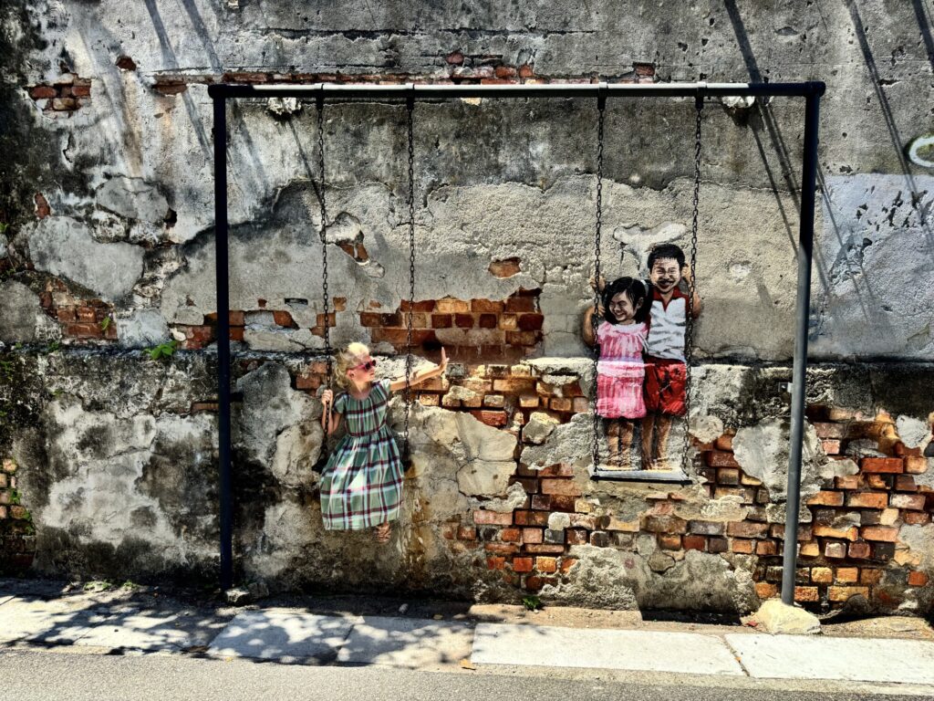 a girl waving to kids who are part of a mural while on a swing