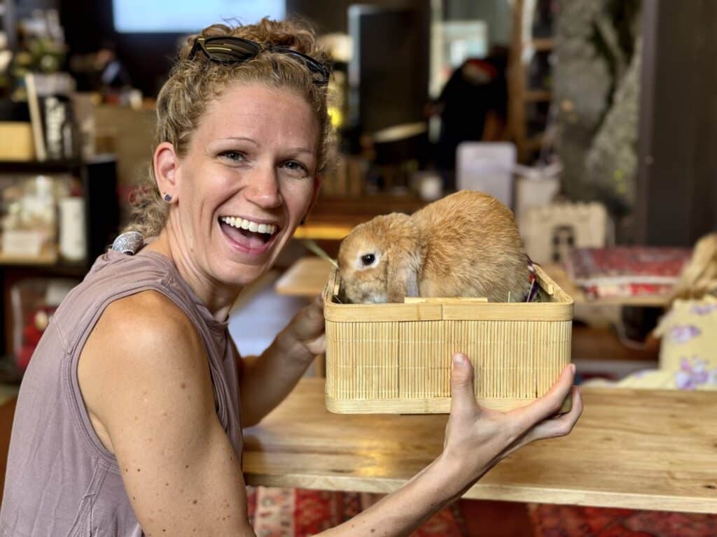 a woman smiling holding a brown rabbit in a box
