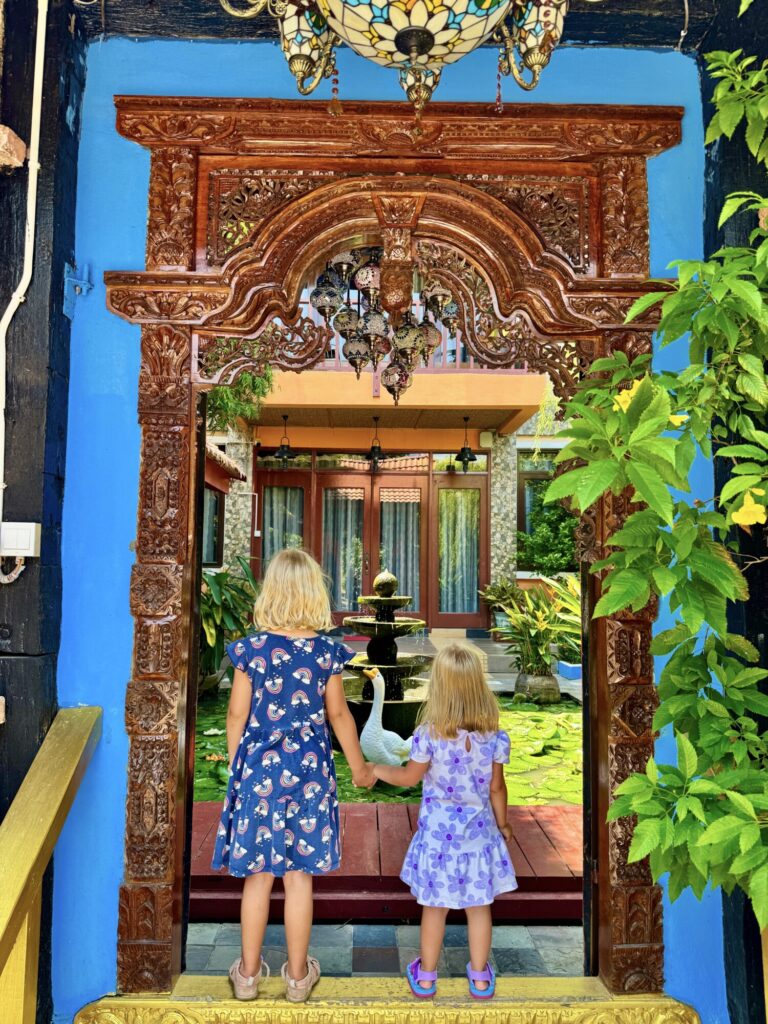 two girls holding hands in a colorful doorway looking into a courtyard with lily pads