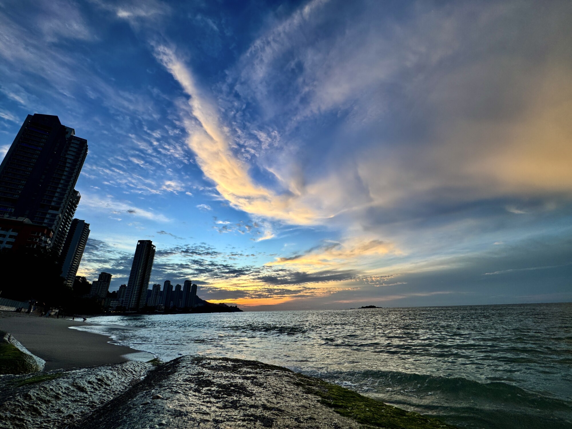 sun setting with wispy clouds on a beach with tall skyscrapers in the mid ground
