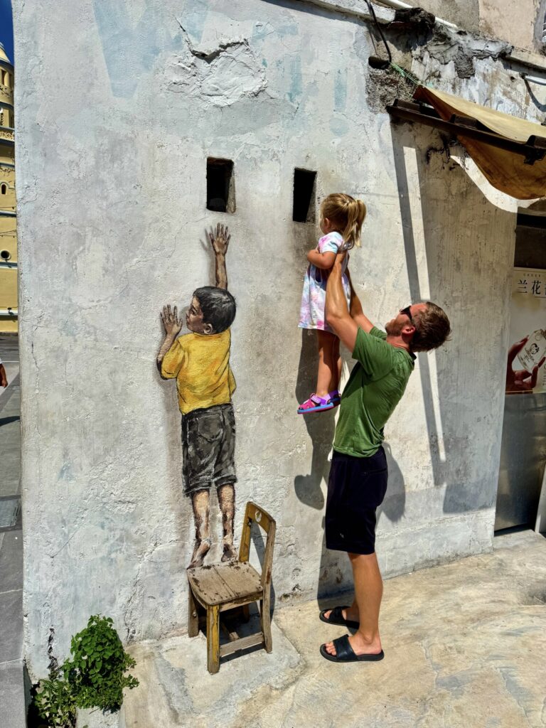 a boy in on a street mural trying to reach up to a window with a girl looking into the window
