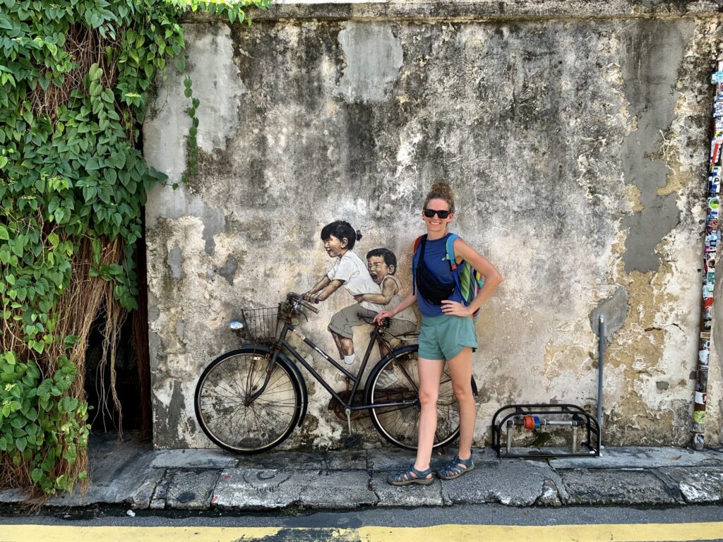 a woman standing next to a street mural depicting two kids on a bicycle