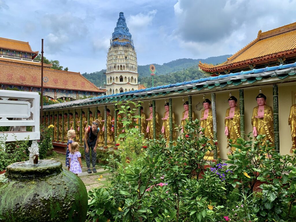 mother and two girls looking at a wall of Buddhist statues in a garden with a fountain