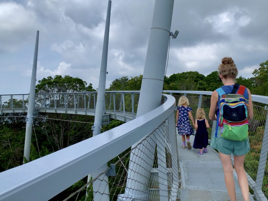 two girls and a mother walking on a bridge walk about the jungle canopy