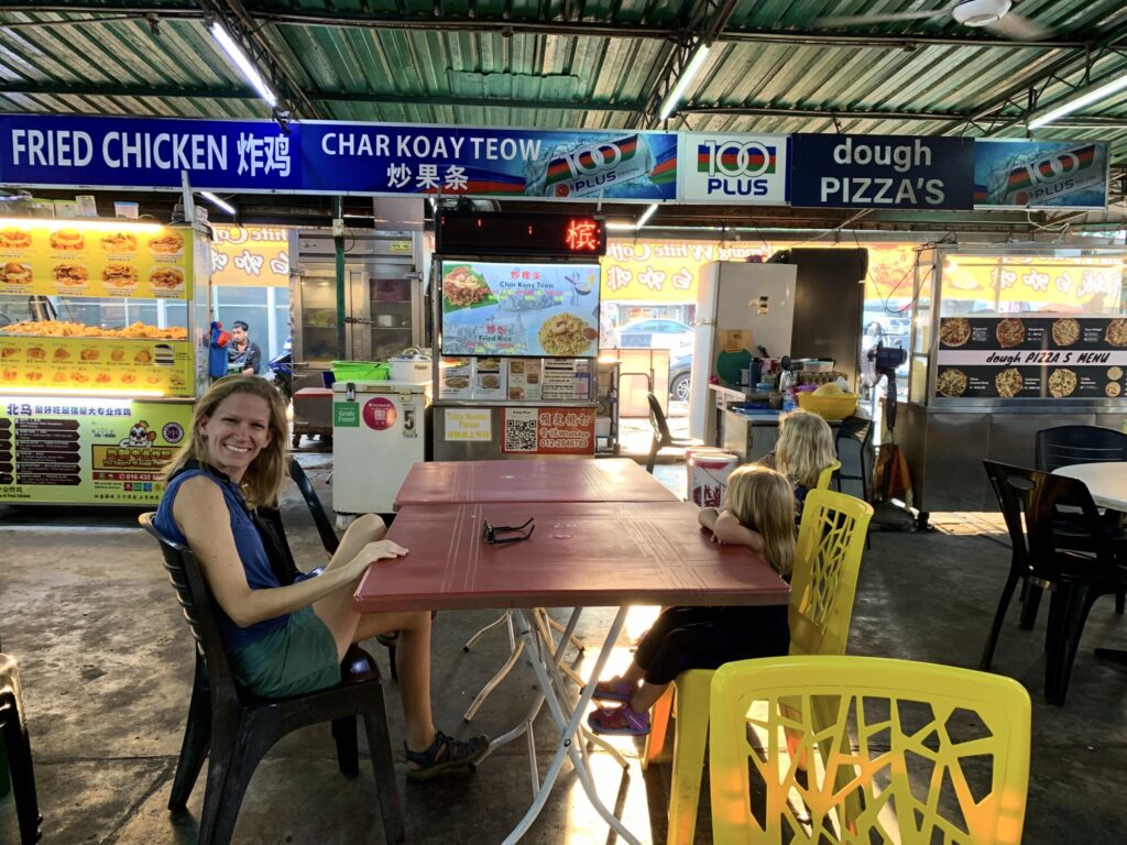 two kids and a mother sitting at a table with multiple food stalls in the background