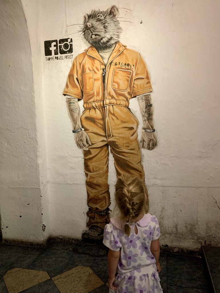 girl looking at a painting of a rat in a prison jumpsuit