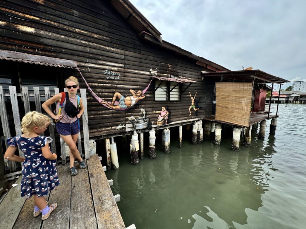 a girl and a woman standing in front of a street art mural on a house over water