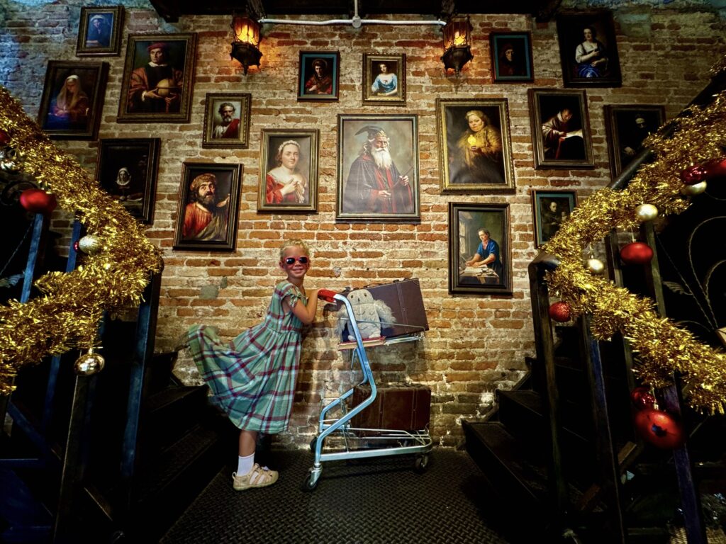 girl pushing a stroller with an owl in front of several Harry Potter character paintings