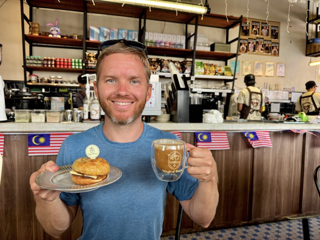 man holding up a pastry and a coffee in a cafe
