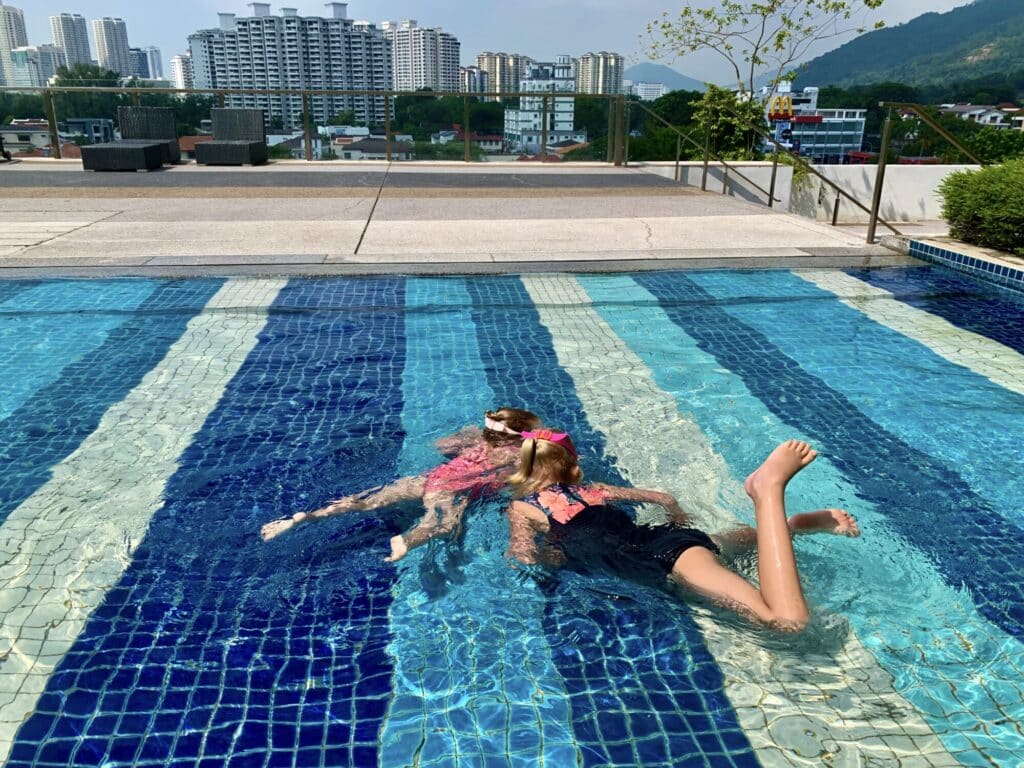 two kids swimming in a shallow pool with a city skyline in the background
