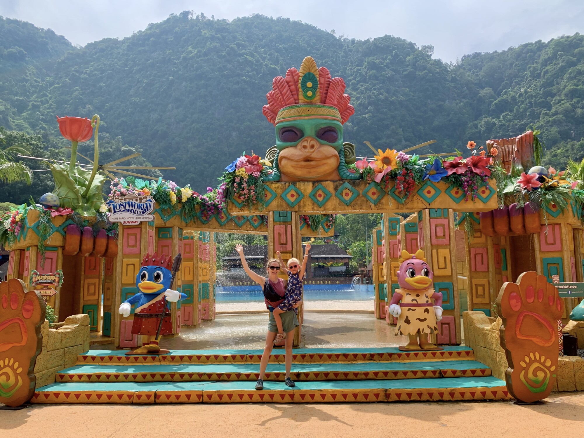 a mom and a daughter posing outside of a colorfully decorated theme park entrance