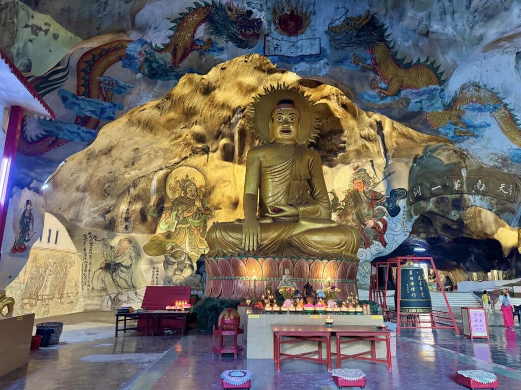 large statue of a golden Buddha in a cave with large dragon paintings on the walls