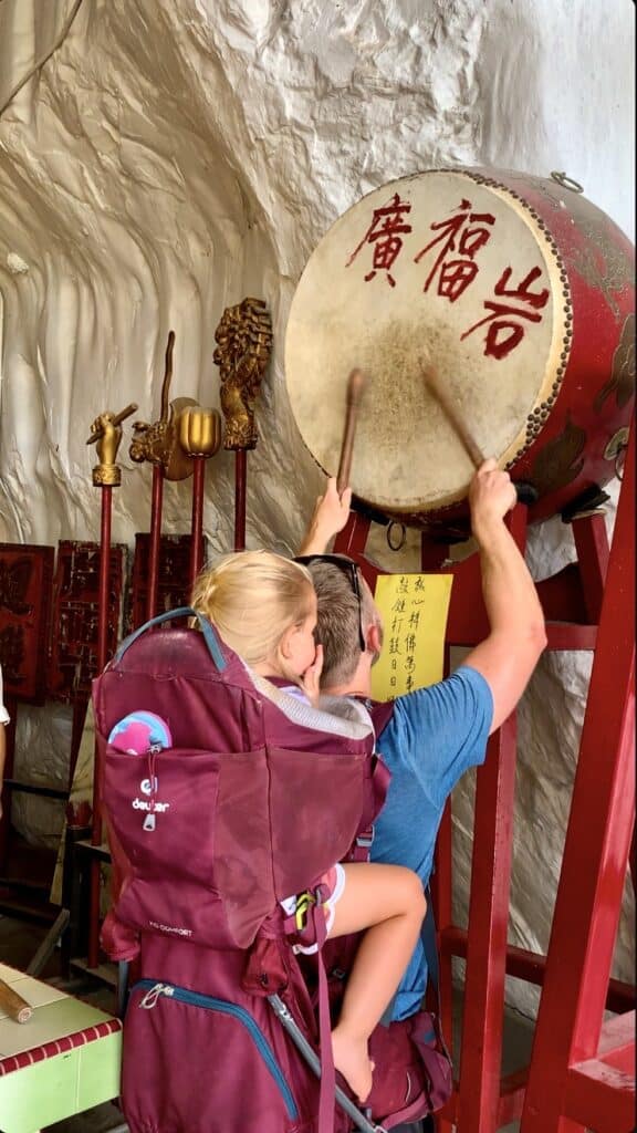 a man banging drums over head with a child in a carrier backpack