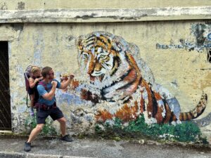 a girl in a carrier backpack and a man acting like they are fighting off a tiger in a mural