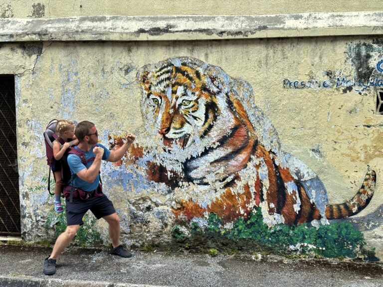 a girl in a carrier backpack and a man acting like they are fighting off a tiger in a mural