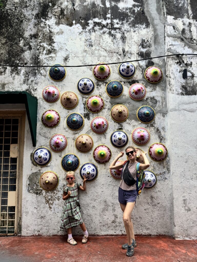 woman and girl posing in front of a wall decorated with conical hats