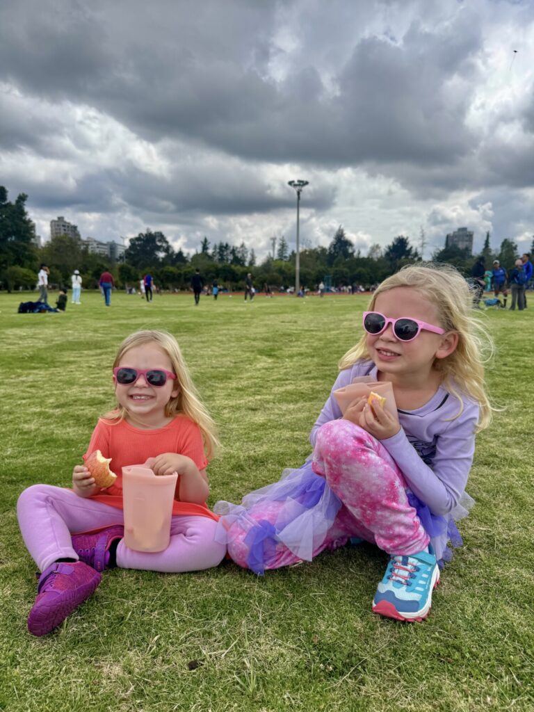 two girls eating a snack on the grass in the park