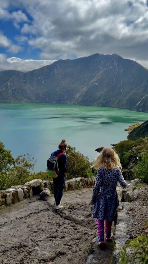 a girl and a woman hiking down a trail to a turquoise lake