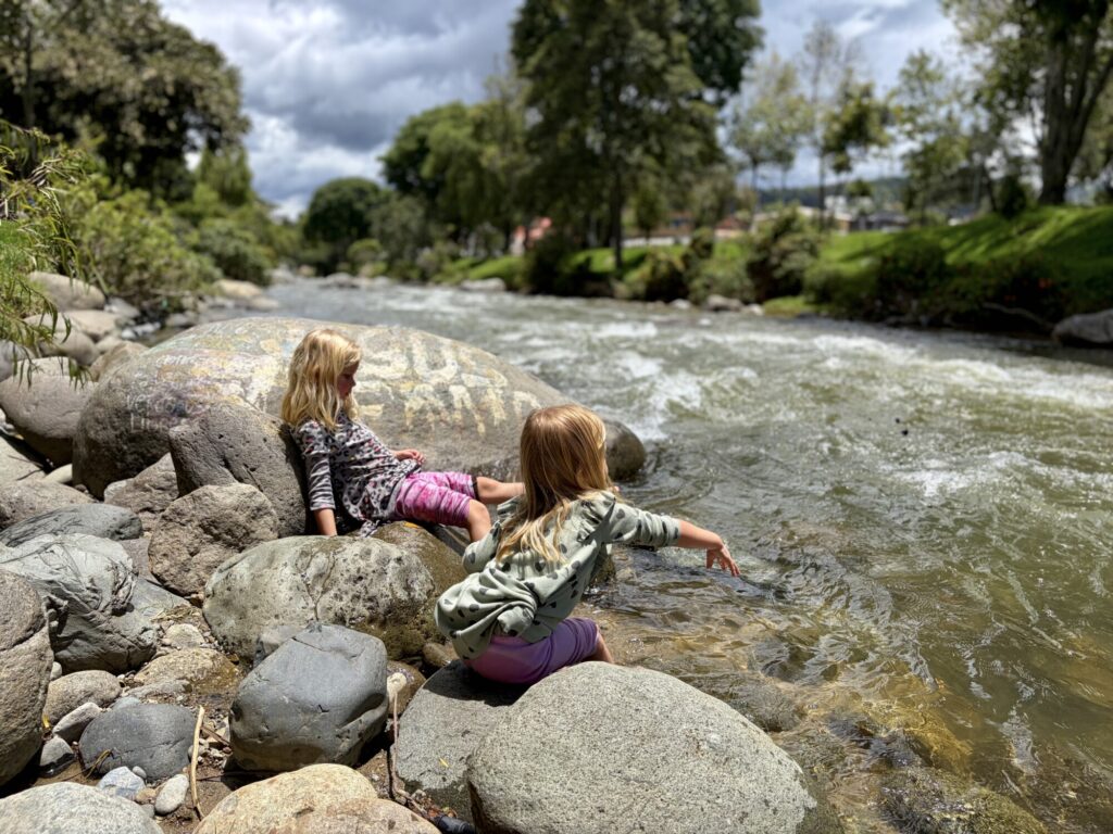 two girls playing by a river with greenery on both sides of the river