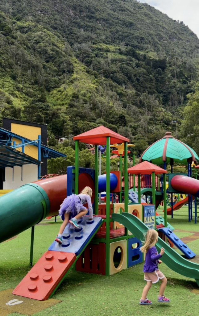 kids running around at a playground with lush mountain greenery in the background