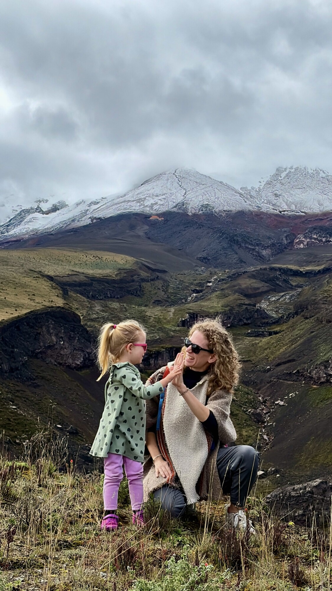 a woman and a child sharing a high five with a volcano in the background