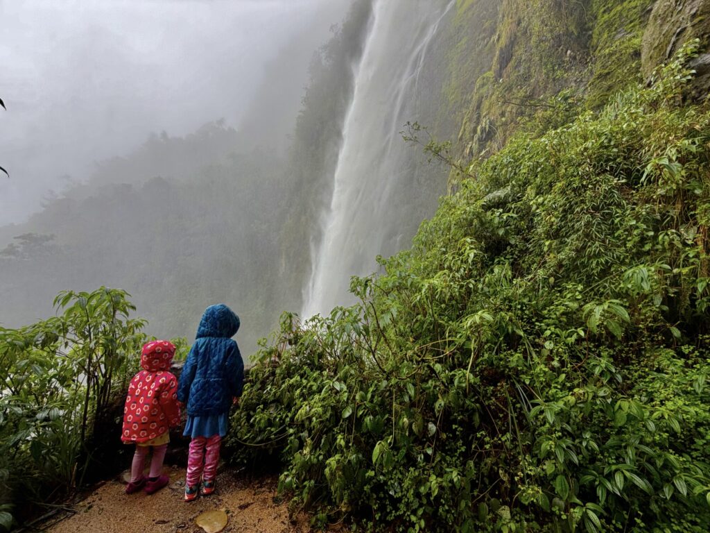 waterfall that is very misty and wet with two kids in rain jackets