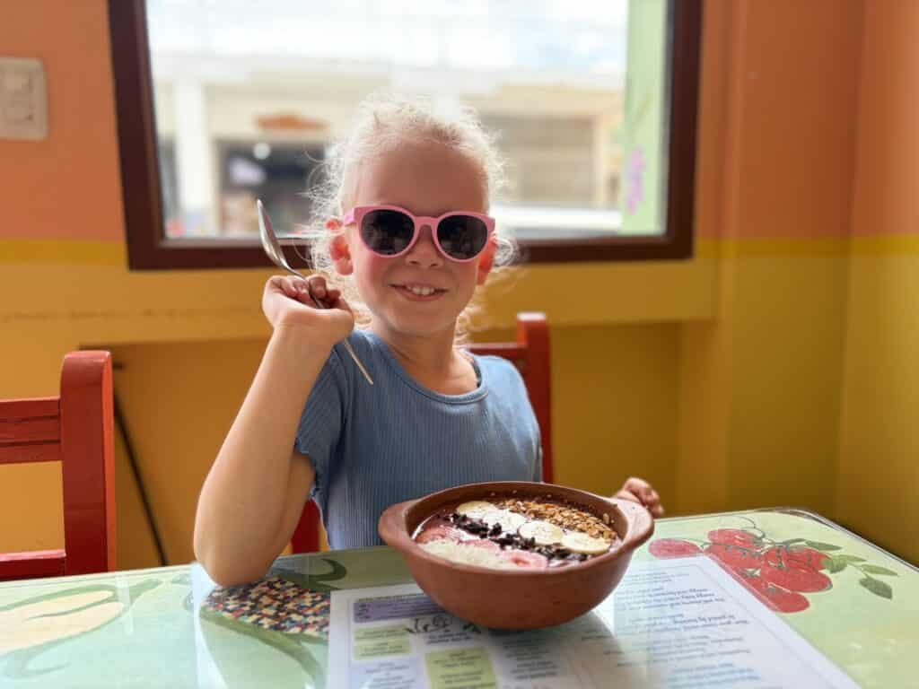a girl sitting at a table with a yogurt bowl with fruit and granola