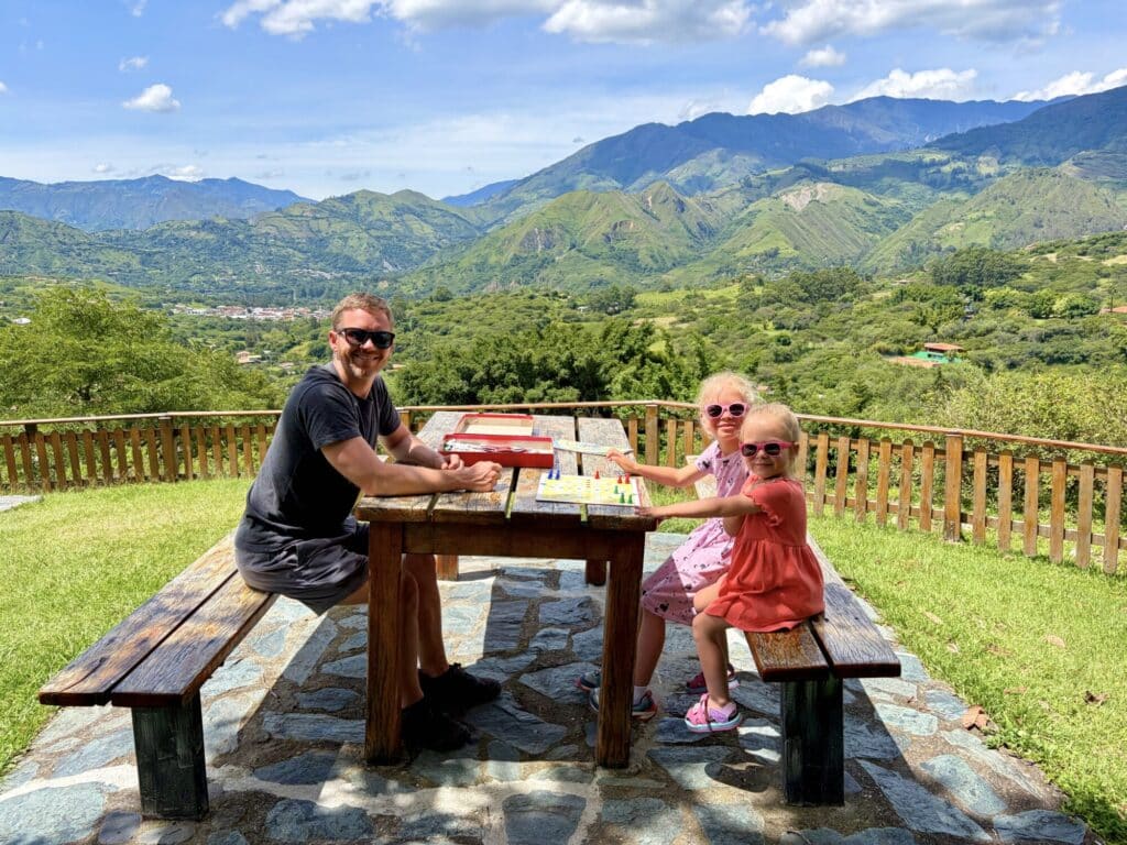 two girls and a father playing a board game outside with mountains in the background
