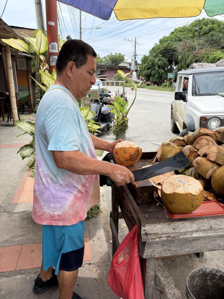a man with a large knife chopping a coconut to drink