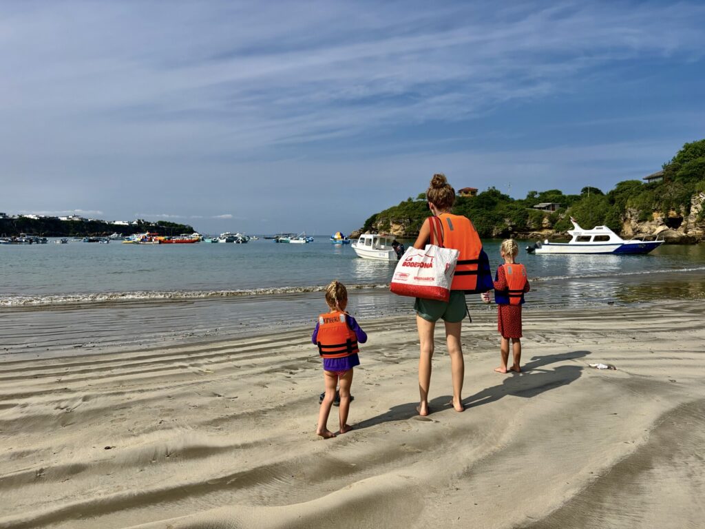 a mother and two kids with life jackets on looking out into a bay that has many colorful boats