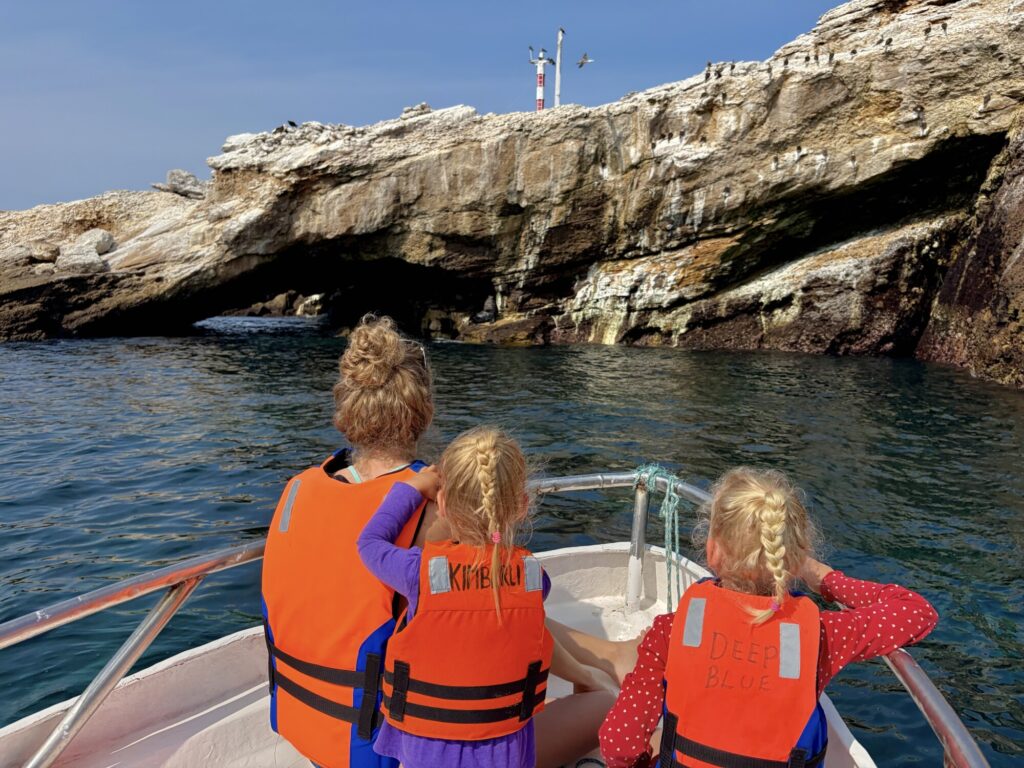 a woman and two kids sitting on the bow of a boat looking at a rock structure with lots of birds