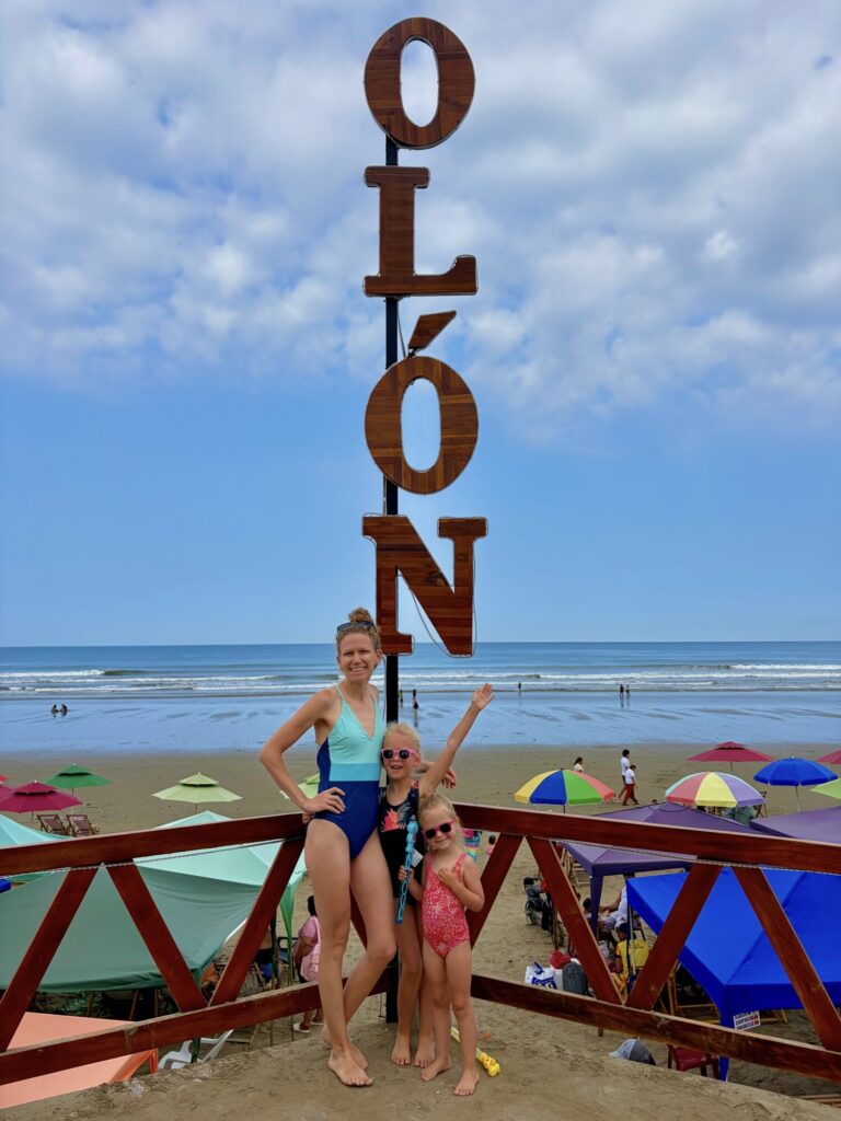a woman and two kids standing on a beach with a sign that says Olon
