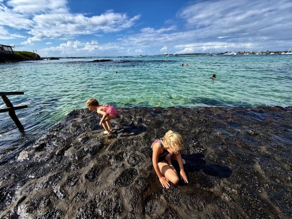 two girls playing on a rock slab by a bay with clear water