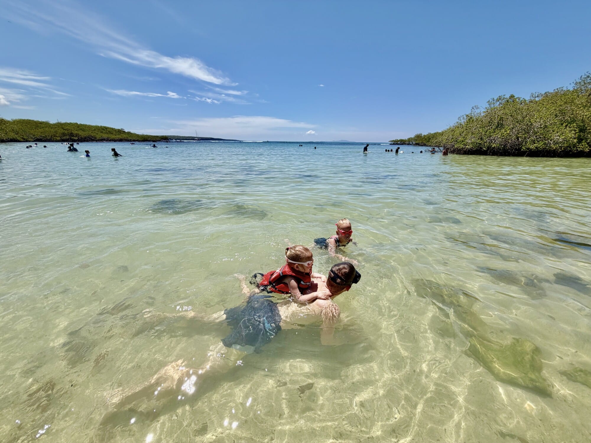 a girl in a life jacket swimming on top of father while using goggles